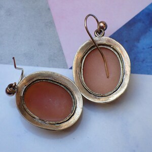 May include: A pair of silver tone earrings with a cameo design. The cameos are oval shaped and have a pink background.