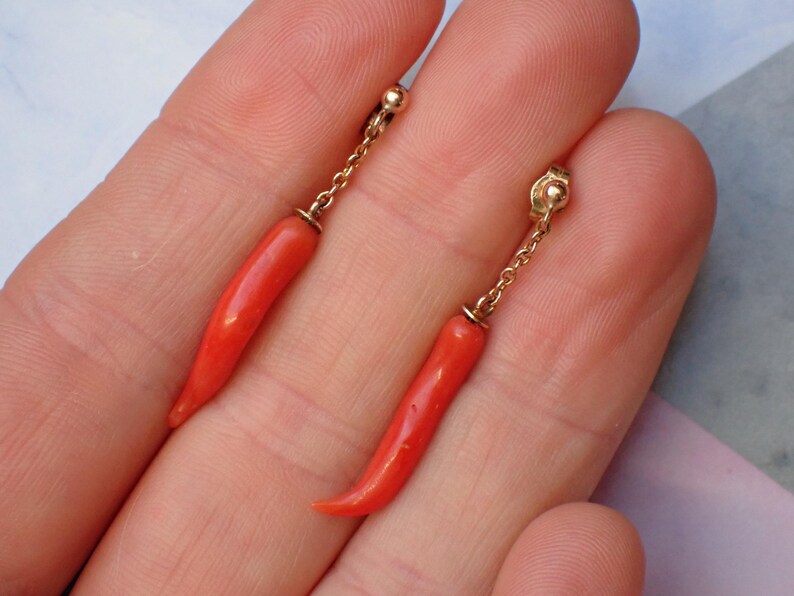 May include: A pair of dangle earrings with red coral chili pepper charms and gold chains.