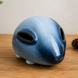 Può includere: Una scultura in ceramica arrotondata con una finitura lucida che sfuma dal blu chiaro al blu navy profondo. L'oggetto presenta due aperture allungate con bordi scuri sulla superficie superiore e poggia su piccoli piedini arrotondati integrati.