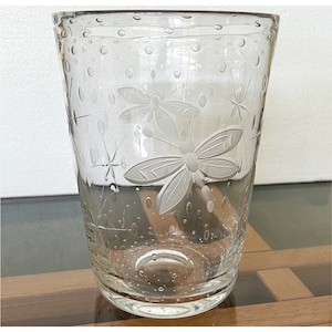 May include: A clear glass vase with a textured surface and etched floral designs. The vase has a round base and a cylindrical shape.
