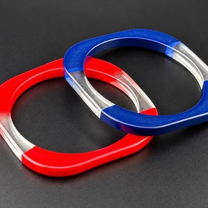 May include: Two square-shaped bangles made of translucent material. One bangle features alternating sections of solid red and clear segments, while the other bangle features alternating sections of solid blue and clear segments.