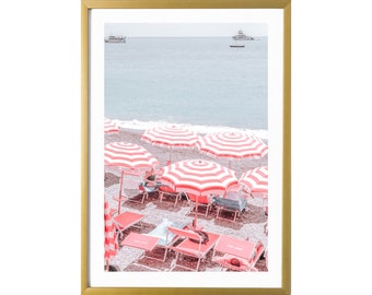 May include: A beach scene with red and white striped umbrellas and red deckchairs on a sandy beach. The sea is in the background.