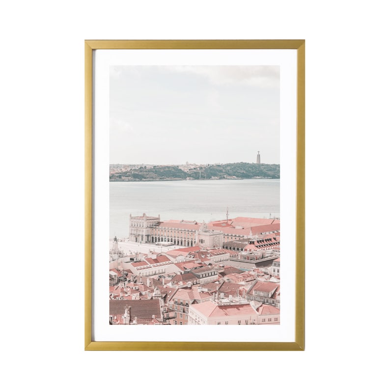 K&ouml;nnte beinhalten: Ein gerahmtes Foto einer Skyline mit einem Fluss im Vordergrund. Die Geb&auml;ude sind in einem blassen Rosaton gehalten und der Himmel ist hellblau. Der Fluss ist hellgrau.