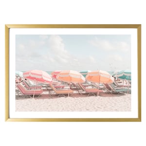 Puede incluir: Una fila de sombrillas de playa coloridas y tumbonas en una playa de arena. Las sombrillas son rosas, naranjas y azules, y las tumbonas est&aacute;n rayadas de rosa, azul y blanco.