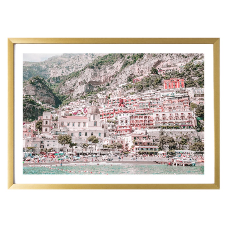 May include: A framed print of a coastal Italian town. The image features colorful buildings cascading down a hillside to a beach. The print is set in a gold-colored frame, adding a touch of elegance to the scenic view.