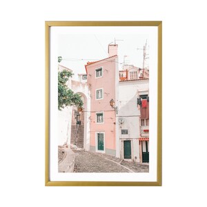 May include: A photo of a narrow, cobblestone street in a European city. The buildings are painted in shades of pink and white, with green doors and windows. There are clothes hanging on a line in the background.