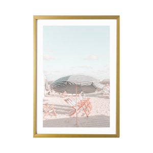 May include: A framed photograph of a beach scene with striped beach umbrellas and red and white beach chairs on a white sandy beach.