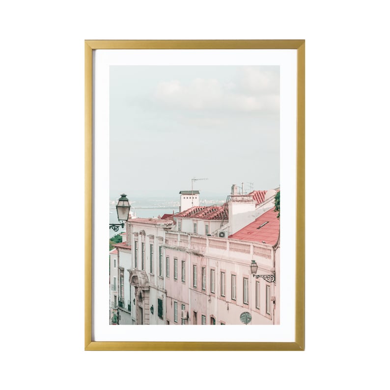 May include: A framed photograph of a street scene in a European city. The buildings are painted in soft pink and white with red tile roofs. A street lamp is visible in the foreground.