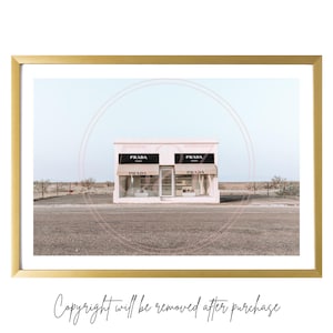 May include: A white building with two storefront windows and a sign that reads "PRADA" on the front. The building is located in a desert landscape with a blue sky in the background.