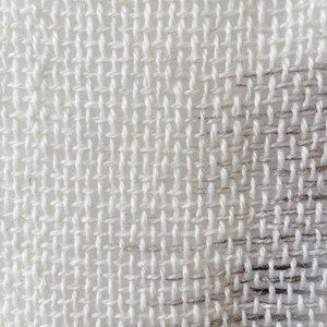 May include: Close-up of a white woven fabric with a subtle pattern. The fabric has a rough texture and a slightly uneven weave.