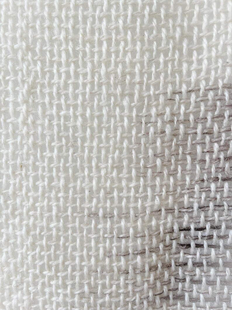 May include: Close-up of a white woven fabric with a subtle pattern. The fabric has a rough texture and a slightly uneven weave.