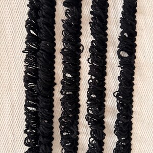Peut inclure: Quatre bandes de tissu noir avec une texture pliss&eacute;e, dispos&eacute;es verticalement sur un fond blanc.