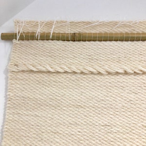 May include: A white woven wall hanging with a natural bamboo rod at the top. The hanging has a textured, woven pattern.