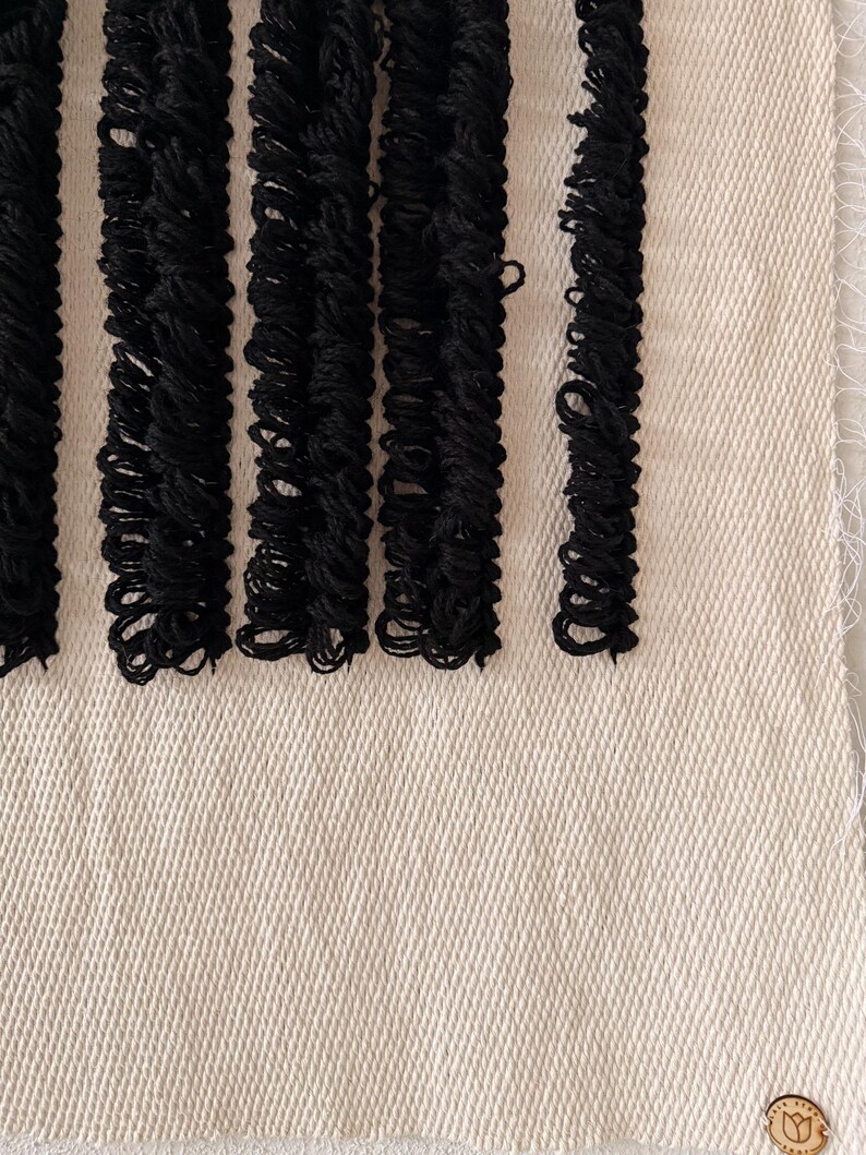 Peut inclure: Une tapisserie murale tiss&eacute;e en noir et blanc avec une bordure en franges. La tapisserie est faite de fibres naturelles et a une surface textur&eacute;e.