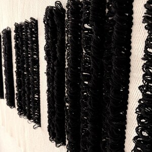 Peut inclure: Tapisserie murale noire et blanche avec une texture tiss&eacute;e. La tapisserie pr&eacute;sente une s&eacute;rie de lignes verticales noires avec un d&eacute;tail de frange.