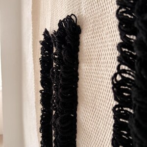 Peut inclure: Une tapisserie murale blanche tiss&eacute;e avec trois bandes de franges noires. Les franges sont faites de fil &eacute;pais et pendent droit.