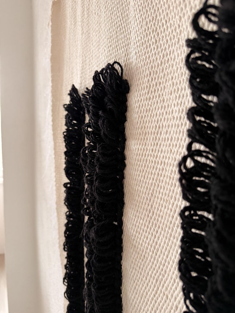 Peut inclure: Une tapisserie murale blanche tiss&eacute;e avec trois bandes de franges noires. Les franges sont faites de fil &eacute;pais et pendent droit.