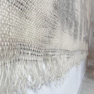 May include: A white woven wall hanging with a fringe border. The hanging has a textured, woven pattern.