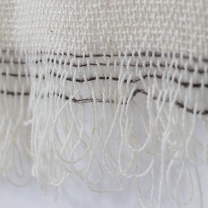 May include: Close-up of a white woven fabric with a fringe border. The fabric has a subtle texture and a thin black line running along the edge.