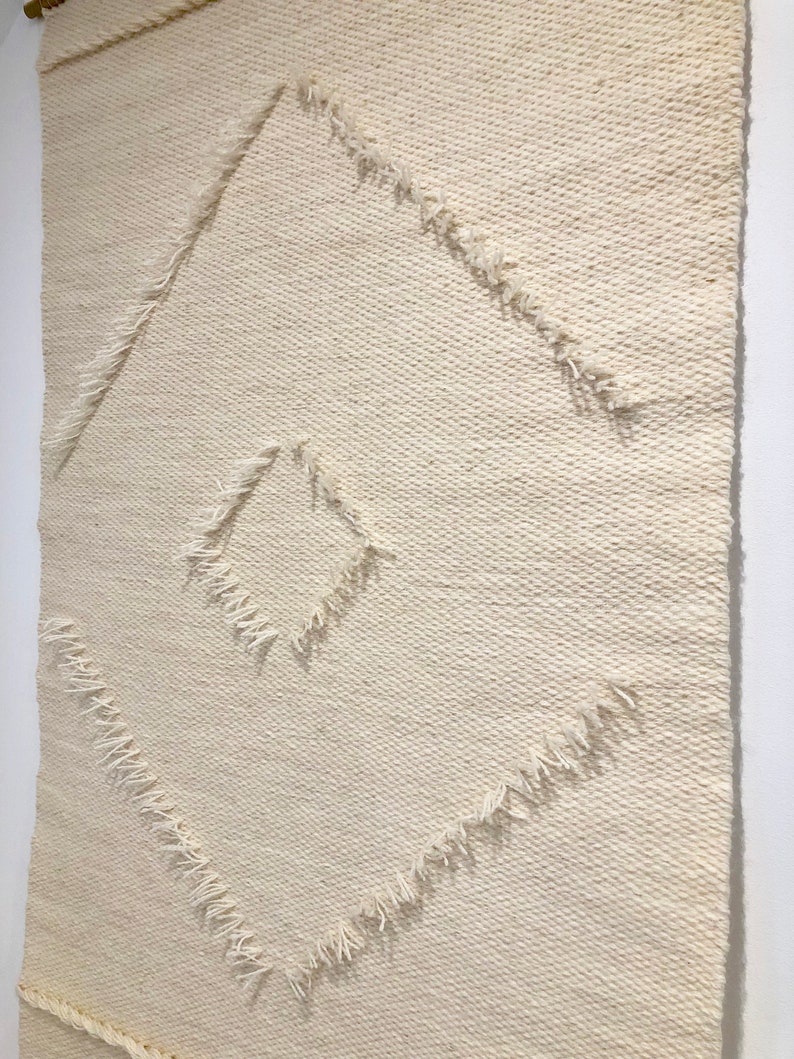 May include: A white woven wall tapestry with a diamond pattern. The diamond is outlined with a fringe detail.
