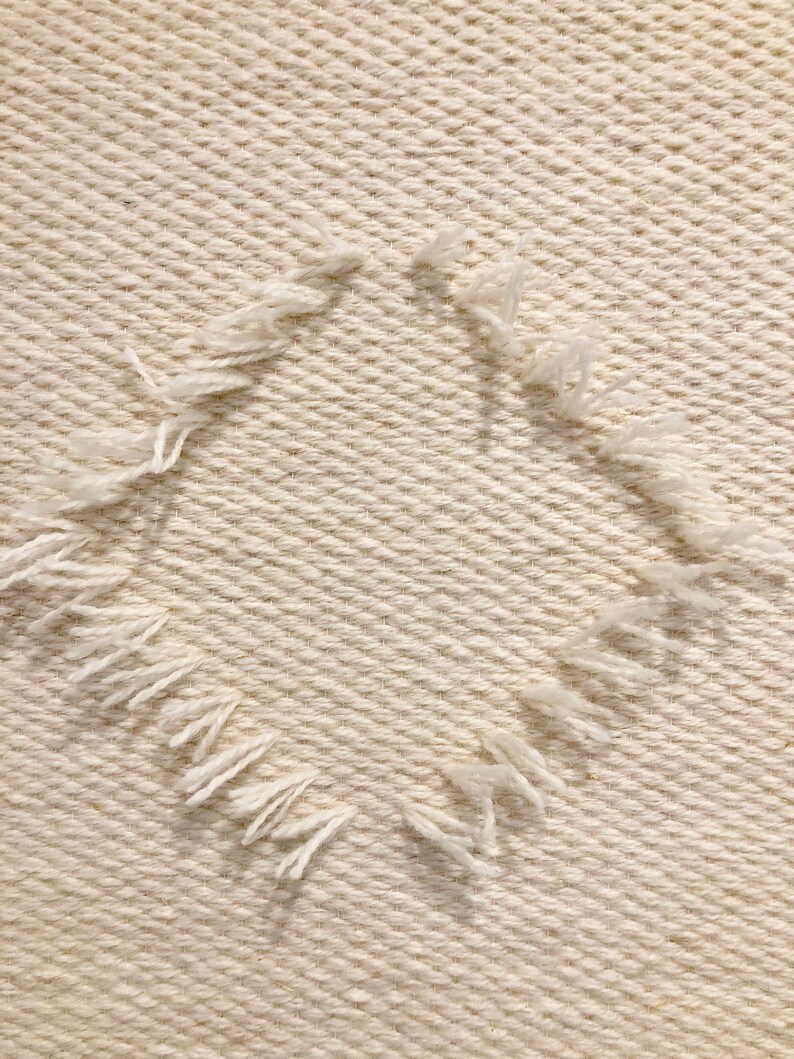 May include: A close-up of a white woven fabric with a frayed edge forming a circle shape.
