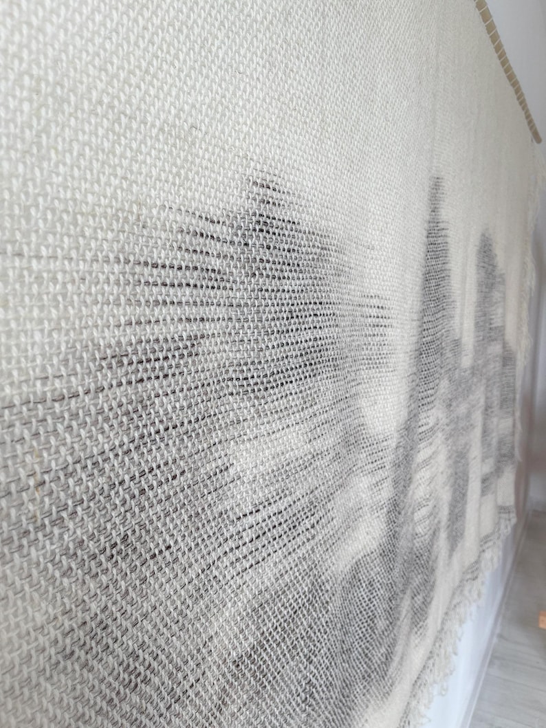 May include: A white woven wall hanging with a black and white abstract design. The design is created by weaving different colored threads together.