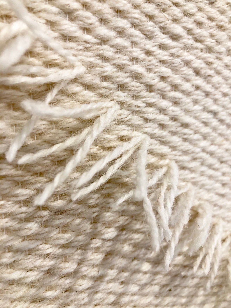 May include: Close-up of a white woven fabric with a textured pattern. The fabric has a frayed edge.