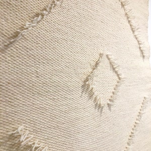 May include: A white woven wall hanging with a diamond pattern. The edges of the diamond shapes are frayed and have a textured look.