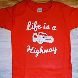 K&ouml;nnte beinhalten: Rotes T-Shirt mit kurzen &Auml;rmeln und einem wei&szlig;en Aufdruck eines Comic-Autos mit dem Text "life is a highway".