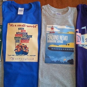 K&ouml;nnte beinhalten: Vier graue T-Shirts mit verschiedenen Disney-Park-Designs. Die Shirts zeigen Bilder von Mr. Toad's Wild Ride, 'it's a small world', Finding Nemo Submarine Voyage und Disneyland. Die Shirts sind alle im gleichen Stil und haben die gleiche Schriftart.