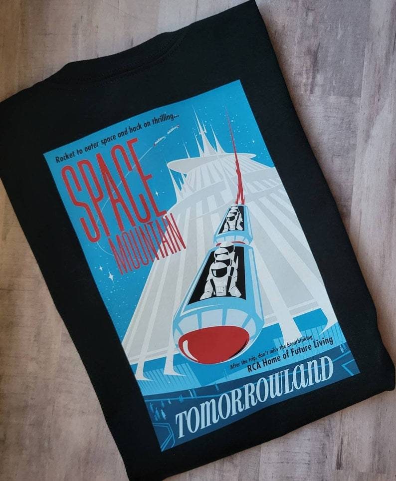 K&ouml;nnte beinhalten: Ein schwarzes T-Shirt mit einer Grafik im Vintage-Stil von Space Mountain, einer Achterbahnfahrt in Disney World. Die Grafik ist in Blau und Wei&szlig; gehalten mit einer roten Rakete und dem Text "Space Mountain" und "Tomorrowland".