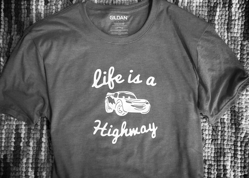 K&ouml;nnte beinhalten: Graues T-Shirt mit einer wei&szlig;en Grafik eines Cartoon-Autos und dem Text "life is a highway".