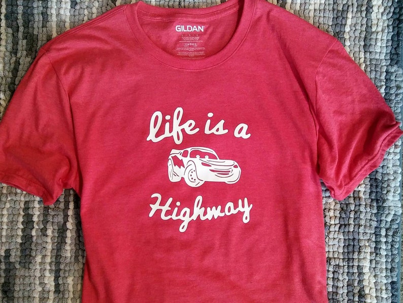 K&ouml;nnte beinhalten: Rotes T-Shirt mit einer wei&szlig;en Grafik eines Cartoon-Autos und dem Text "life is a highway".