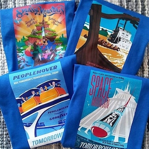 K&ouml;nnte beinhalten: Vier blaue T-Shirts mit Vintage-Illustrationen von Disney-Vergn&uuml;gungsparkfahrten. Die Shirts zeigen Bilder von Splash Mountain, Peoplemover, Space Mountain und einer Holzf&auml;llerfahrt. Die Shirts haben den Text "Tomorrowland" und "Ride Tomorrow's Transportation...Today" aufgedruckt.