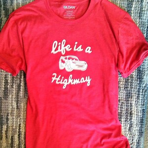 K&ouml;nnte beinhalten: Rotes T-Shirt mit einer wei&szlig;en Grafik eines Cartoon-Autos und dem Text "Life is a Highway".