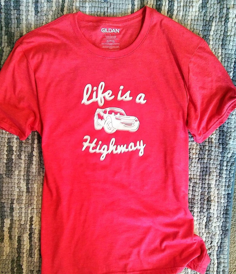 K&ouml;nnte beinhalten: Rotes T-Shirt mit einer wei&szlig;en Grafik eines Cartoon-Autos und dem Text "Life is a Highway".