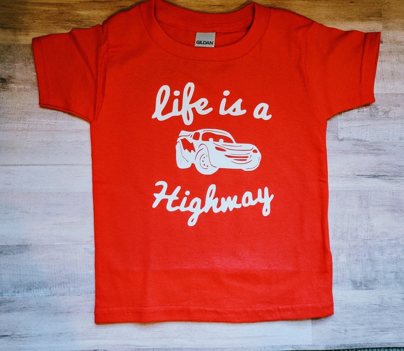 K&ouml;nnte beinhalten: Rotes T-Shirt mit kurzen &Auml;rmeln und einem wei&szlig;en Aufdruck eines Comic-Autos mit dem Text "life is a highway".