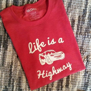 K&ouml;nnte beinhalten: Rotes T-Shirt mit einer wei&szlig;en Grafik eines Cartoon-Autos und dem Text "life is a highway".