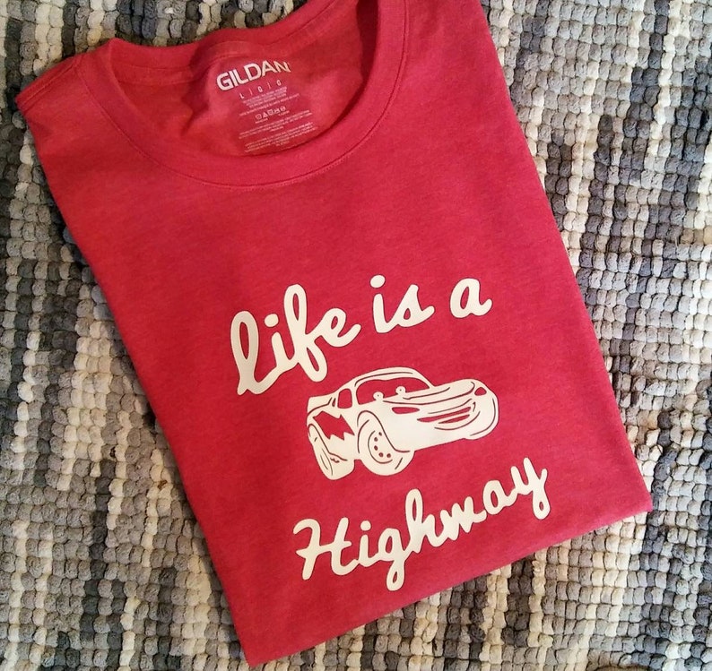 K&ouml;nnte beinhalten: Rotes T-Shirt mit einer wei&szlig;en Grafik eines Cartoon-Autos und dem Text "life is a highway".