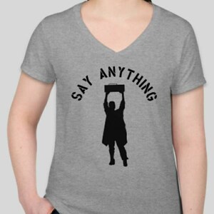 May include: A gray V-neck t-shirt with the text "SAY ANYTHING" in a black semi-circle around a silhouette of a person holding a boombox above their head.
