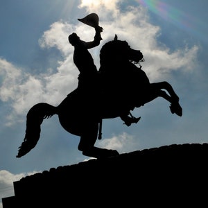 Könnte beinhalten: Silhouette einer Statue einer Person auf einem Pferd, mit der Sonne, die hell im Hintergrund scheint.