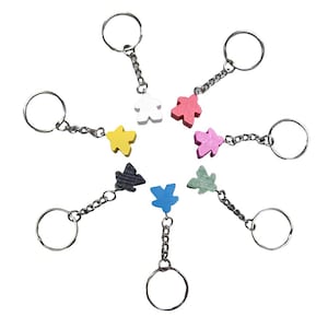 May include: Seven keychains with different colored wooden figures attached. The figures are shaped like a person and are in the colors black, white, yellow, pink, red, blue, and green.