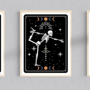 Op de afbeelding: Drie zwart-wit illustraties van skeletten in verschillende yoga-houdingen. Elke illustratie is ingelijst in een licht houten lijst en geplaatst tegen een zwarte achtergrond met witte sterren, manen en andere hemellichamen.