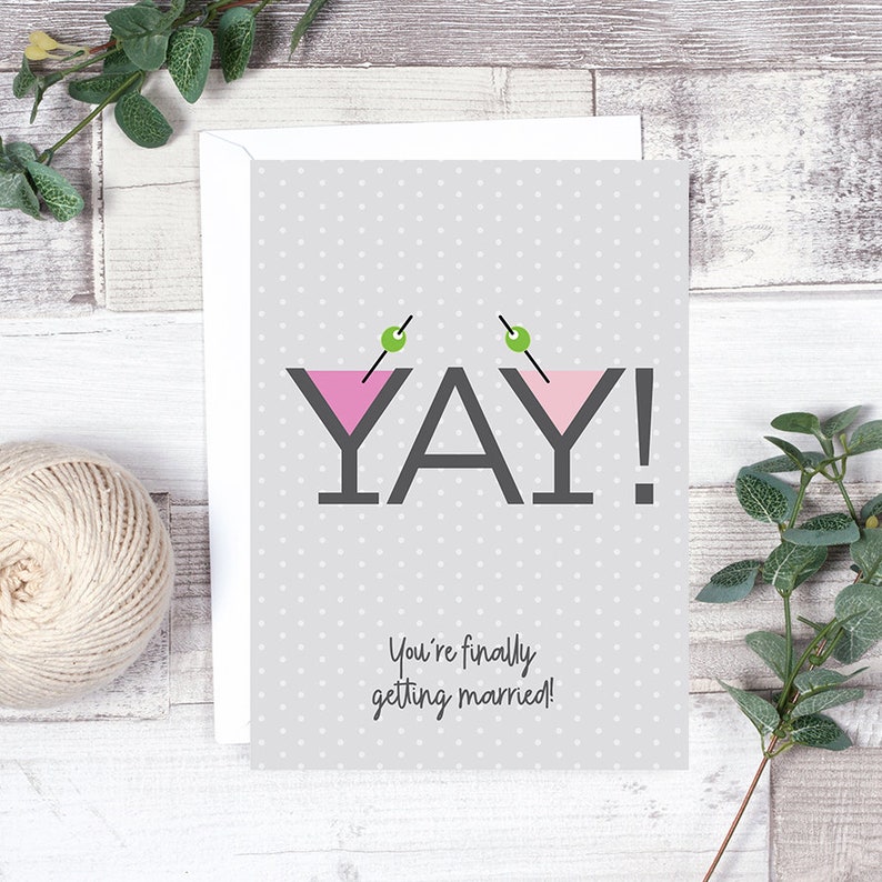 May include: A gray card with white polka dots and the text "YAY!" in black with two pink martini glasses with green olives on top. The text "You're finally getting married!" is below the main text.
