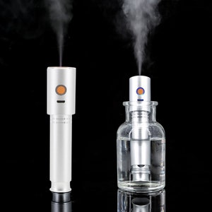 May include: Two silver aromatherapy diffusers with steam emitting from the top. One diffuser stands alone, the other is inside a clear glass bottle filled with water. Each has a colored button and a small indicator light.