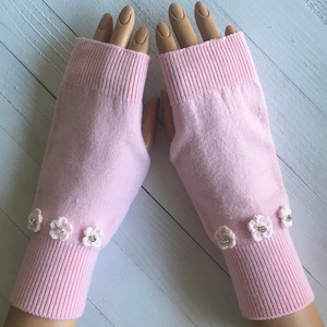 May include: A pair of pink fingerless gloves with white crocheted flowers and rhinestones on the cuffs.