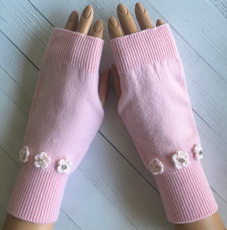 May include: A pair of pink fingerless gloves with white crocheted flowers and rhinestones on the cuffs.