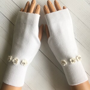 May include: White fingerless gloves with white flower embellishments with rhinestone centers.