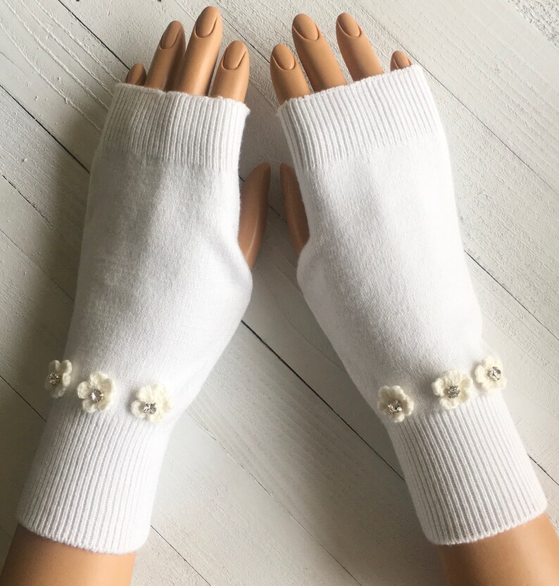 May include: White fingerless gloves with white flower embellishments with rhinestone centers.