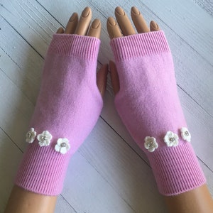 May include: A pair of pink fingerless gloves with white crocheted flowers on the cuffs.